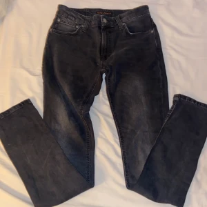Svarta jeans från Nudie Jeans, W28 L32 skinny lin - Snygga svarta jeans från Nudie Jeans med klassisk femficksdesign och diskret broderi på bakfickorna. Jeansen har raka ben och normal passform, tillverkade i mjukt denimtyg. Perfekta för dig som gillar stilrena och tidlösa jeans. Modellen på jeansen är skinny lin.