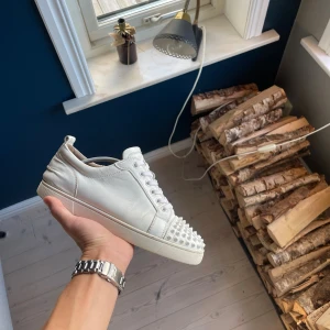 Christian Louboutin  - Säljer ett par vita sneakers från Christian Louboutin i skinn med coola nitar över tån. Skorna har snörning, platt sula och en klassisk låg siluett. Perfekta för dig som vill sticka ut med en edgy detalj på fötterna. Dustbags medföljer 