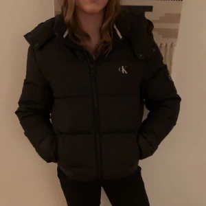 Svart pufferjacka Calvin Klein Jeans XS - Svart pufferjacka från Calvin Klein Jeans med logga på bröstet, ärmen och insidan. Jackan har huva, dragkedja framtill och är vadderad för extra värme. Perfekt för kalla dagar! Jag fick jackan av min kille som också använt den, alltså passar för båda könen🩷
