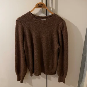 Brun stickad tröja från KappAhl - Mysig brun stickad tröja från KappAhl med rund halsringning och långa ärmar. Tröjan har en klassisk passform och är perfekt för kyliga dagar. Materialet är mjukt och ger en avslappnad vibe. Den är lite nopprig.