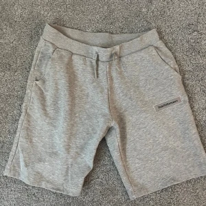 Grå shorts från Peak Performance - Snygga grå shorts från Peak Performance med mjuk bomullskänsla. De har elastisk midja med snörning, två sidofickor och en bakficka. Perfekta för chill dagar eller träning. Diskret logga framtill för en clean look.