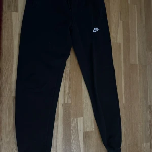 Svarta mjukisbyxor från Nike (barn storlek L, men passar storlek S kvinnor) - Svarta mjukisbyxor från Nike med klassisk logga på låret. Byxorna har resår och snörning i midjan samt muddar vid bensluten. Tillverkade i mjukt bomullsmaterial för maximal komfort. Perfekta för chill eller träning.