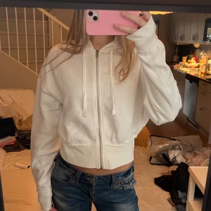 Vit croppad hoodie med dragkedja - Säljer en vit croppad hoodie med dragkedja framtill och snörning vid huvan. Perfekt att slänga på över ett linne eller t-shirt 🫶🏼 Aldrig använd och passar både XS och S!