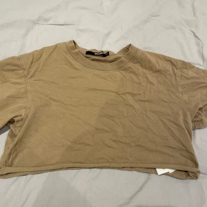 Beige croppad t-shirt från Bik Bok - Säljer en enkel och snygg beige croppad t-shirt från Bik Bok. T-shirten har rund hals och korta ärmar, perfekt för en chill och avslappnad stil. Passar dig som gillar basic och neutrala färger.