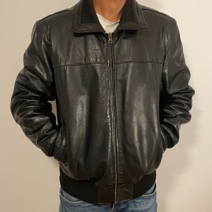 Svart skinnjacka  - Snygg svart skinnjacka med klassisk krage och dragkedja framtill. Jackan har ribbade muddar vid ärmslut och nederkant, samt två sidofickor. Perfekt för dig som gillar en stilren och tidlös look. Passformen är normal och jackan är långärmad. Pris kan diskuteras vid snabb affär.