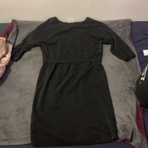 Svart glittrig klänning True Spirit - Svart glittrig klänning från True Spirit i storlek M. Klänningen har trekvartsärm, markerad midja och en rak, kort siluett. Perfekt för dig som vill sticka ut med lite extra glitter. Enkel och snygg design som passar till många tillfällen. Jätte fin klänning att använda till nyår har inte använt den så mycket 