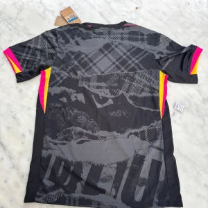 Chelsea fotbollströja  - Snygg fotbollströja från Nike  i svart och grått med rutig mönster och coola detaljer i neonrosa och gult. Kortärmad modell med V-ringning och broderad lejonlogga på bröstet. Tillverkad i lätt och ventilerande polyester.