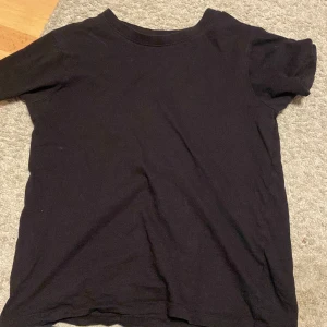 Svart t-shirt från Kappahl - En basic svart t-shirt från Kappahl i storlek 146/152. Klassisk rund halsringning och korta ärmar. Perfekt till jeans eller shorts. Gjord i mjuk bomull för skön känsla hela dagen.