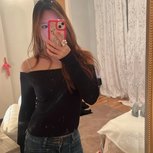 Svart offshoulder topp från Dazy - Svart långärmad offshoulder topp från Dazy. Snygg, tight passform med raka linjer över axlarna och smal siluett. Tunn och stretchig, perfekt att styla med jeans eller kjol. Enkel och stilren design utan mönster eller detaljer.