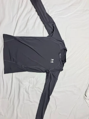 UNDER ARMOUR COMPRESSION - Bilderna visar en grå långärmad tröja från Under Armour, tillverkad i syntetmaterial och designad för träning. Tröjan har en rund hals och logotypen syns både fram och bak. Passar perfekt för sportaktiviteter