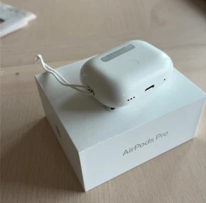 AirPods Pro - Apple AirPods Pro med laddningsetui och originalförpackning. Skicket är begagnat med synliga repor och mindre slitage på etuiet. Levereras med snöre för enkel transport. Perfekt för trådlös musik och samtal med aktiv brusreducering.