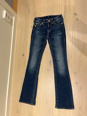 True Religion Bootcut Jeans  - Säljer ett par snygga blå jeans från True Religion, modell BECCA low Rise Bootcut. Jeansen har klassisk femficksdesign, kontrastsömmar och ikoniska broderade bakfickor. Materialet är slitstarkt denim med en cool tvätt och bootcut-ben. Pris kan diskuteras🥰🥰