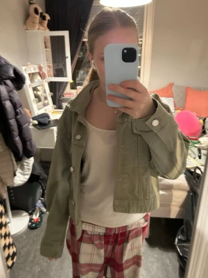 Grön jeansjacka med knappar - Snygg ljusgrön jeansjacka med klassisk krage och silvriga knappar framtill. Jackan har en rak passform och är croppad i modellen. Super fint skick! Storlek är M men den passar mig som är 155 och liten.