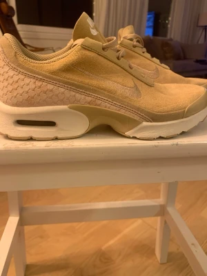 Beige Nike Air Max sneakers mocka - Säljer ett par nya beige Nike Air Max sneakers med snyggt hexagonmönster på hälen och klassisk Nike-logga. Ovandelen är i mocka och har snörning framtill. Skorna har en vit och beige sula med synlig Air-enhet för extra komfort. Perfekt för dig som gillar stilrena och unika sneakers.