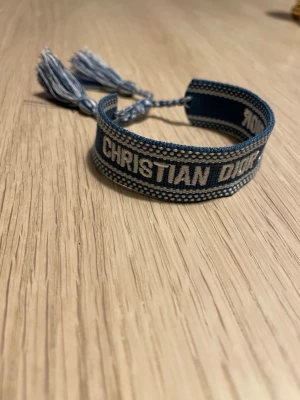 Dior armband - Säljer ett schysst blått armband från Christian Dior med broderad logga och tofsar.