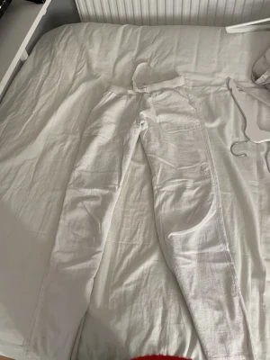 Vita linnebyxor med snörning - Säljer ett par vita linnebyxor med skön passform och snörning i midjan. Byxorna har raka ben och praktiska fickor framtill. Perfekta för varma dagar och chill stunder. Materialet är linne som ger en luftig och fräsch känsla.