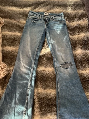 Bootcut jeans med slitningar, ljusblå - Säljer ett par ljusblå bootcut jeans från 157 med snygga slitningar och hål på ena benet. Klassisk femficksmodell med dragkedja och knapp. Jeansen har en cool tvätt och är tillverkade i jeansmaterial. Perfekt för dig som gillar en avslappnad och trendig stil.