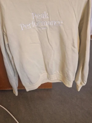 Gul sweatshirt från Peak Performance - Säljer en beige sweatshirt från Peak Performance i storlek L. Tröjan har broderad logga på bröstet och är långärmad med ribbade muddar vid ärmslut och nederkant. Perfekt för chill dagar och enkel att matcha med jeans eller joggers.