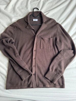 Filippa K tröja - Säljer en brun stickad kofta från Filippa K i storlek S. Koftan är tillverkad i en mjuk blandning av ekologisk bomull och linne, har långa ärmar, klassisk krage, bröstficka och knäppning framtill. Perfekt för lager på lager under höst och vår.
