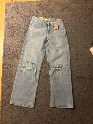 Levi's Superlow Loose jeans, ljusblå -  Aldrig använda. Säljer ett par Levi's Superlow Loose jeans i ljusblå tvätt med låg midja och avslappnad passform. Byxorna har breda ben och slitna detaljer med hål på båda knäna. Klassisk femficksmodell och tillverkade i jeansmaterial. Perfekt för dig som gillar en chill och trendig look.