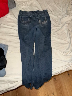 Blå bootcut jeans från Romwe, S - Snygga blå bootcut jeans från Romwe i storlek S. Jeansen har klassisk femficksdesign och coola detaljer med glittriga broderier på bakfickorna. Perfekt passform med normal midja och tillverkade i mjukt jeansmaterial.