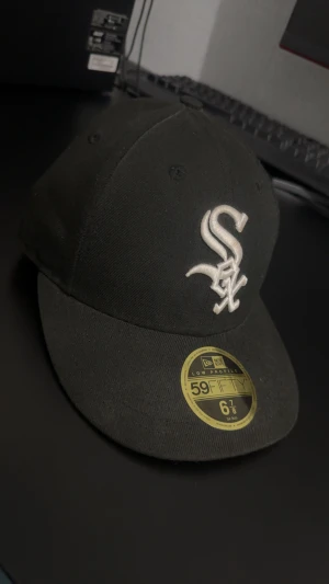 Svart New Era 59FIFTY White Sox keps - Säljer en svart New Era 59FIFTY keps med White Sox-logga broderad i vitt framtill. Klassisk flat brim och låg profil. Insidan har märkning och etiketter, materialet är bomull. Perfekt för dig som gillar streetwear och sport. Kontakta gärna för funderingar🤩