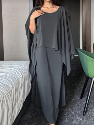 Mörkgrå långklänning med volang - Säljer en mörkgrå långklänning med lös passform och breda, svepande ärmar. Klänningen har volangdetaljer längs sidorna och en rund halsringning. Materialet är mjukt och faller snyggt, perfekt för dig som gillar en chill och stilren look.