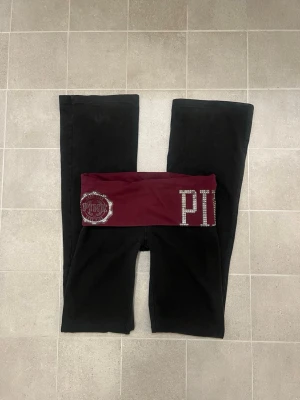 Svarta bootcut byxor från PINK - Snygga trendiga svarta bootcut byxor från PINK Victorias Secret med bred vinröd midja dekorerad med glittrande stenar och stora PINK-loggor. Lite urtvättade och några stenar saknas. Storlek XS.