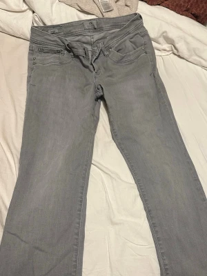 Grå jeans från LTB Blue Addiction - Säljer ett par grå jeans från LTB Blue Addiction med klassisk femficksdesign och snygga detaljer på bakfickorna. Jeansen har dragkedja och knapp framtill, raka ben och normal passform. Perfekt för dig som gillar stilrena och enkla jeans.