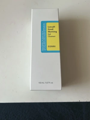 COSRX Low pH Good Morning Gel Cleanser - En mild gelrengöring från COSRX med låg pH-nivå, perfekt för att rengöra huden utan att torka ut. Kommer i en vit och blå förpackning med gul etikett, innehåller 150 ml. Innehåller botaniska ingredienser och är tillverkad i Korea.