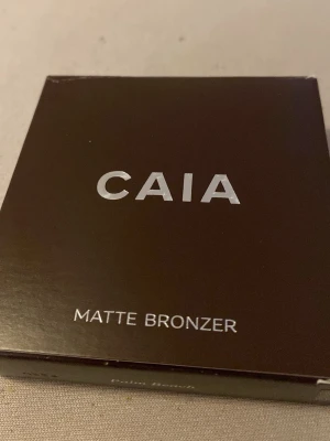 CAIA Matte Bronzer Palm Beach - Snygg matt bronzer från CAIA i färgen Palm Beach. Kommer i en stilren brun fyrkantig förpackning med silvrig text. Innehåller bland annat mango- och kakaosmör för en mjuk känsla. Perfekt för att ge ansiktet en solkysst look. Den är swatchad en gång bara, Den är i nytt skick, min mamma köpte fel färg till mig i julklapp tyvärr så därför säljer jag:)