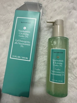 NATURIUM Niacinamide Cleansing Gelée - NATURIUM Niacinamide Cleansing Gelée 3% i en genomskinlig pumpflaska på 210 ml. Gelen är lätt grönaktig och kommer i en stilren turkos förpackning. Innehåller 3% niacinamid för en fräsch och rengjord känsla.