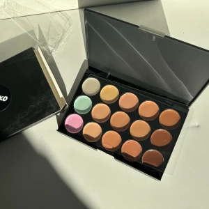 Concealerpalett med 15 nyanser - Snygg concealerpalett med 15 olika nyanser, inklusive beige, bruna, gröna, gula och rosa toner. Perfekt för att täcka ojämnheter, highlighta och korrigera hudtonen. Kommer i en smidig svart plastförpackning med genomskinligt lock.