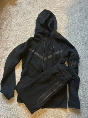 Nike tech fleece-ställ - Nike tech fleece-ställ svart i mycket fint skick. Tröjan är XS vuxenstorlek och byxorna är XL barnstorlek. Båda passar någon med storlek 170 eller XS vuxen.