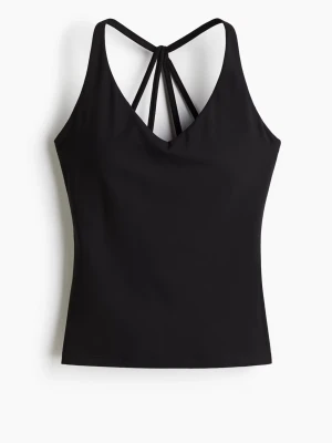 Svart träningslinne - Svart träningslinne med smala axelband som korsas i ryggen och ger en snygg detalj. Toppen har en v-ringad hals och är i storlek S. Ny med prislapp utan defekter. 