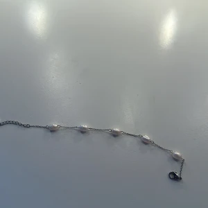 Silverarmband med vita pärlor. HELT OANVÄNT ARMBAND - Ett stilrent armband i silverfärgad kedja med sex ovala vita pärlor jämnt fördelade längs länken. Perfekt för dig som gillar en clean och elegant look med en touch av klassisk vibe.