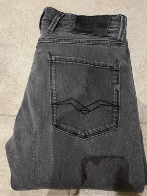 Replay Anbass grå slim jean - Säljer ett par Replay Anbass jeans i snygg mörkgrå tvätt. Slim fit-modell med klassiska fem fickor och diskreta detaljer på bakfickorna. Jeansen har normal midja och raka ben, tillverkade i mjuk och stretchig denim för skön passform. 31/31