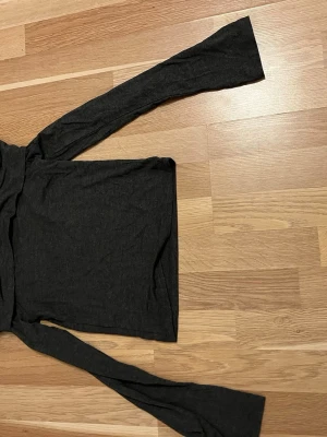 Svart axelbandslös tubtopp med långa ärmar - Säljer en svart tubtopp med långa ärmar. Toppen är axelbandslös och har en enkel, stilren design i mjukt material. Perfekt för dig som gillar minimalistiska plagg med en modern touch. Yogapants material, tröjan är mörkgrå.