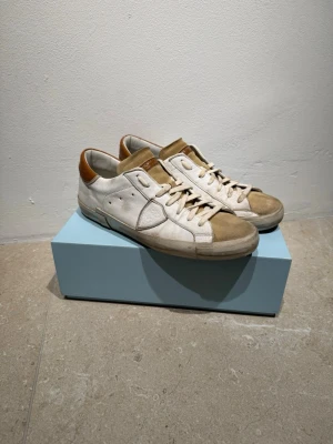Philippe Model vita och beige sneakers - Snygga sneakers från Philippe Model i vitt och beige med bruna detaljer på hälen och plösen. Skorna har snörning, rund tå och platt sula med tydlig Philippe Model-logga undertill. Materialmix av skinn och mocka,           Obs!!, Pris kan diskuteras!!
