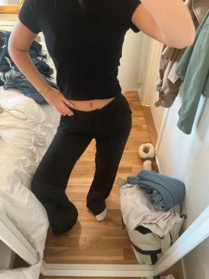 Svarta kostymbyxor  - Säljer ett par svarta kostymbyxor med breda ben och klassisk midja. Byxorna har hällor för bälte och stängs med knapp och dragkedja. Perfekt för dig som gillar en clean och stilren look med lite extra attityd.