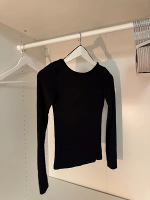 Svart långärmad topp med rund hals - En stilren svart långärmad topp med rundad halsringning. Öppen / lägre rygg🤩 Tight passform och mjukt, stretchigt material som sitter snyggt på kroppen. Perfekt att matcha med jeans eller kjol för en clean look.