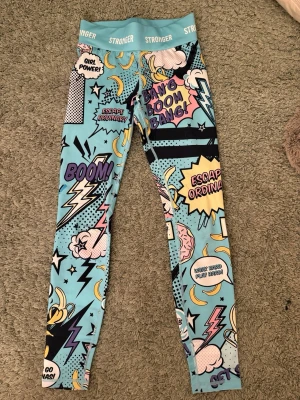 Stronger leggings med serietidningsmönster - Säljer ett par snygga tränings tights från stronger🩵 tightsen är i jätte bra skick och säljer eftersom de är både för små och inte riktigt min stil 