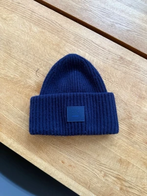 Mörkblå acne studios mössa - Säljer denna mörkblåa Acne studios mössa då den inte kommer till användning. Den är nästan inte använd och är i mycket bra skick