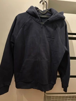 Mörkblå hoodie med dragkedja - Snygg mörkblå hoodie från Peak Performance med dragkedja framtill och två stora fickor. Klassisk huva och ribbade muddar vid ärmar och nederkant. Tillverkad i mjukt bomullsmaterial som är skönt att ha på sig. Perfekt för en avslappnad och stilren look. Mycket bra skick. Storlek S