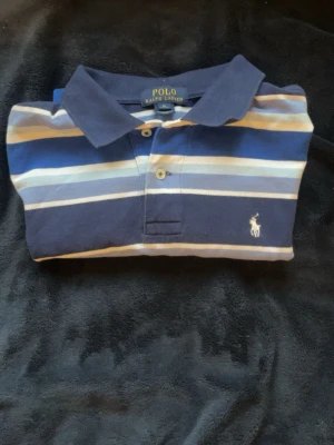 Ralph Lauren piké - Snygg pikétröja från Polo Ralph Lauren i marinblått, vitt och ljusblått. Skicket är bra, utan fläckar hål eller annat. Storleken 10-12, men den sitter som XS. Jag är 180 och väger 66. Den sitter tight på mig. Så den är nog perfekt om du är runt 170-175 och runt 60 kg. Kan skicka mått vid inteessse. 