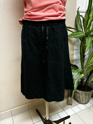 Svart linne kjol med snörning i midjan - Enkel svart kjol med snörning i midjan och avslappnad passform. Kjolen har en rak siluett och är knälång, perfekt för en stilren look. Tillverkad i ett mjukt tyg som känns bekvämt hela dagen.