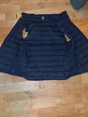 Svart dunväst från Parajumpers - Snygg svart dunväst från Parajumpers med quiltad design och dragkedjor på sidorna. Västen har en klassisk ståkrage och den ikoniska Parajumpers-loggan vid nacken. Perfekt för lager-på-lager och streetwear.