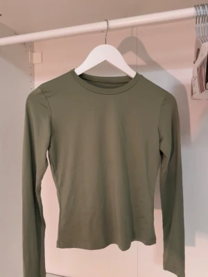 Olivgrön långärmad topp - En stilren olivgrön långärmad topp med rund halsringning. Toppen har en tajt passform och är tillverkad i ett mjukt, stretchigt material som sitter skönt mot kroppen. Perfekt att matcha med jeans eller kjol för en enkel och snygg look🤩 Står ej storlek men skulle uppskatta XS-S