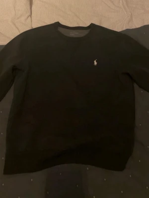 Ralph Lauren Sweatshirt - En Svart Polo Ralph Lauren Sweatshirt som jag köpte på Vinted och säljer då den var för stor för mig. Förutom att taggen uppe vid nacken är sliten som syns på bilden, så finns det inga defekter och tröjan är som ny. Storlek M. Priset kan diskuteras.