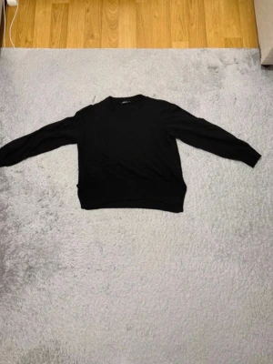 Svart stickad tröja Gina Tricot - En klassisk svart stickad tröja från Gina Tricot med rund halsringning och långa ärmar. Tröjan har ribbade muddar vid ärmslut och nederkant, perfekt för lager-på-lager-stil.